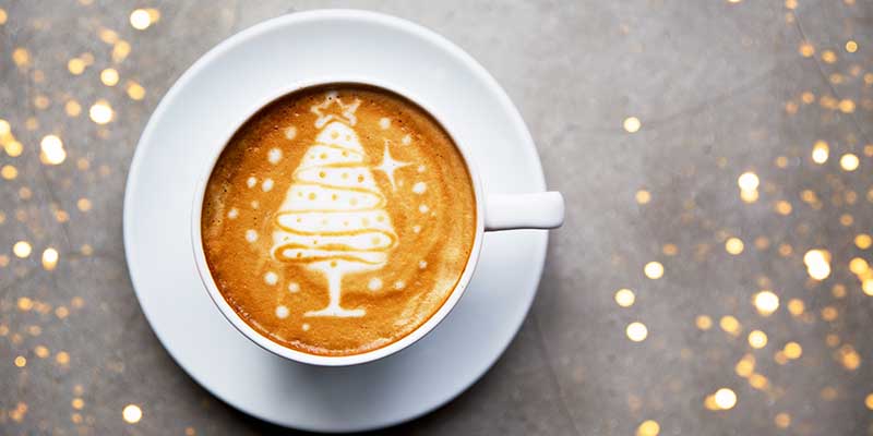 Tasty cappuccino with Christmas tree latte art with some blurred lights. Holiday concept.